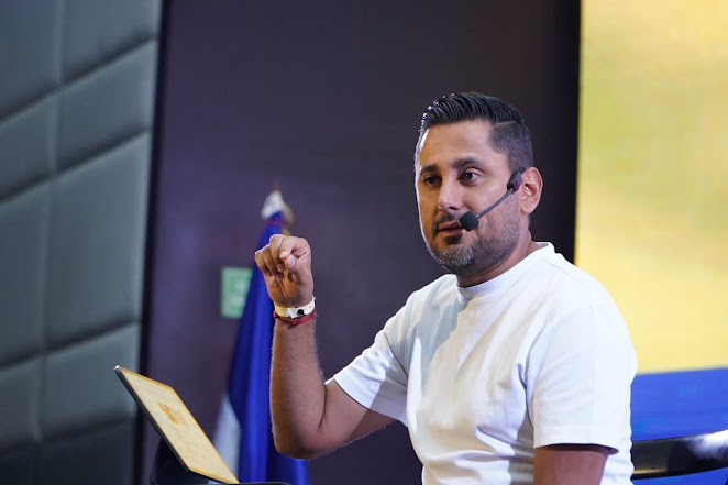 Carlos Sánchez desafía el poder con su conferencia en la Cumbre de Comunicación Política en Punta Cana Imagen abstracta con tonos oscuros y formas.